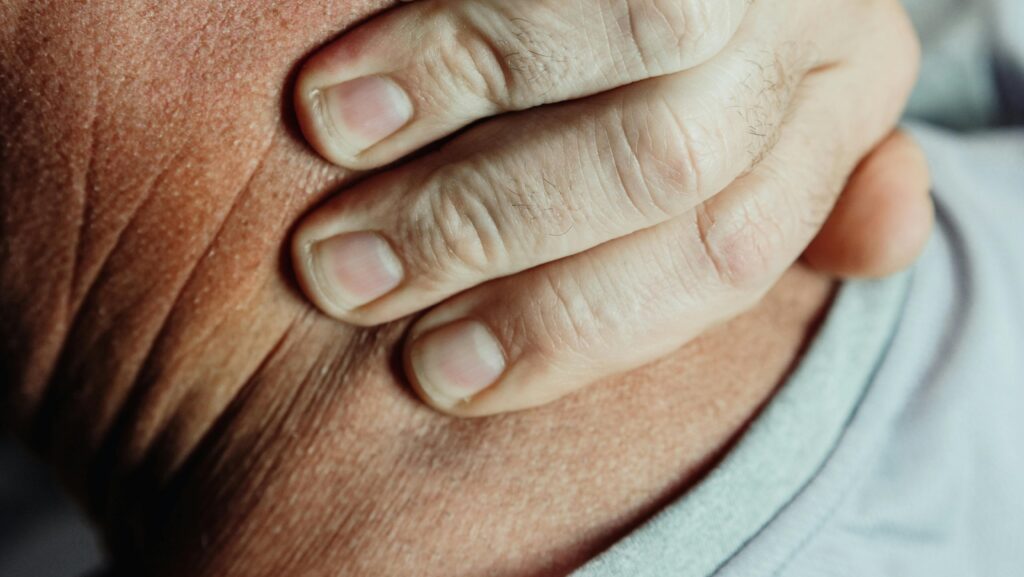 Close-up of a person's hand holding their shoulder, indicating pain or discomfort.